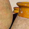 Image of Close-up of rustic ceramic pots with a textured beige body and a glossy mustard-yellow glazed rim, set outdoors on a light sandy surface.