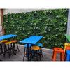 Image of Artificial White Tropics Vertical Garden Wall Panels installed on a concrete wall in an outdoor setting with tables and chairs