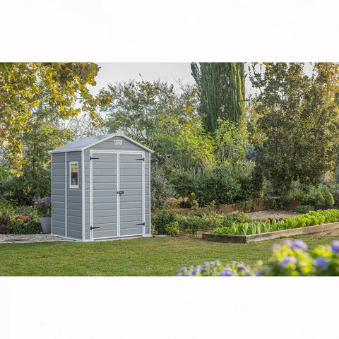 Gray garden shed in a garden setting with trees and plants.
