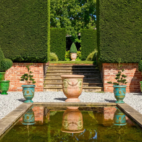 Garden scene with decorative urns, steps, and hedges.