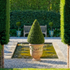 Image of Decorative urn with a topiary in a garden setting with a pond and bench.