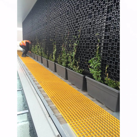 man installing pots at the bottom of an atlantis facade wall, with climbing plants growing up the trellis