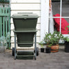 Image of Green hungry bin on wheels outside a house with plants around

