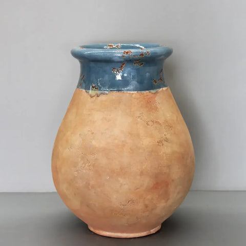 A handmade ceramic vase with a rounded, bulbous body in a warm, textured terracotta orange-brown glaze, and a contrasting blue glazed neck with small orange floral details, set against a neutral gray background.