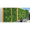 Image of Artificial Green Meadows 1m x 1m Plant Wall Panel UV Stabilised installed on a concrete wall with wooden accents styled with figurines and displayed beside a swimming pool