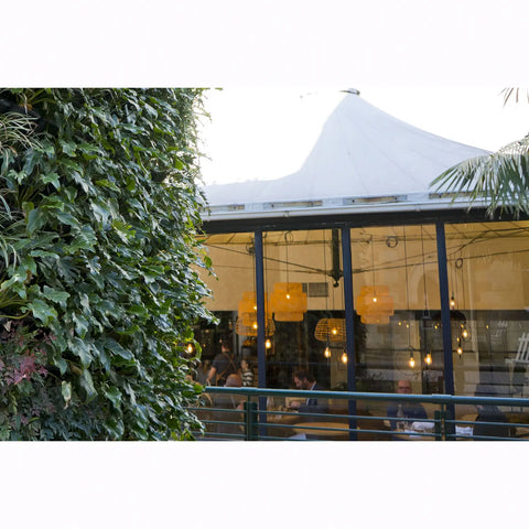 Outdoor seating area with people dining under a white tent, surrounded by vertical greenery.
