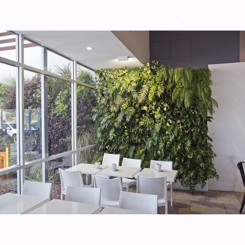 Modern interior with white tables and chairs against a green living wall.