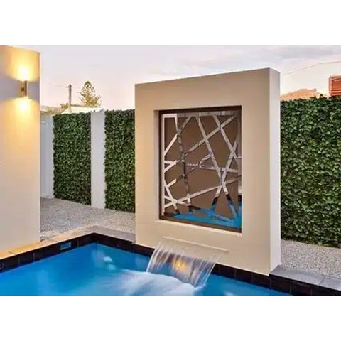 Modern backyard pool with a waterfall cascading from a large beige wall surrounded by the Artificial Ivy Leaf Hedge 1m x 1m Plant Wall Screening Panel UV Protected