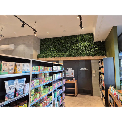 Specialty store interior featuring the Artificial Ivy Leaf Hedge Panels above doors, bright track lighting, neatly stocked shelves, and a mix of concrete and textured walls