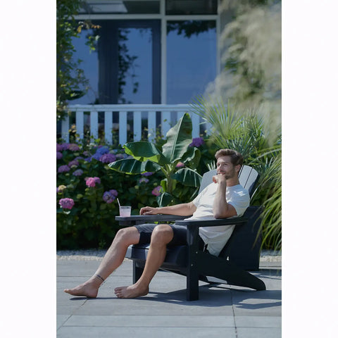 Man relaxing on a modern graphite adirondack chair with a garden and house in the background