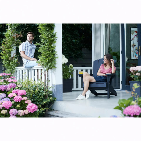 Two people sitting on a porch with flowers and plants around.