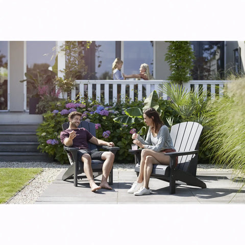 Two people sitting on Adirondack chairs in a garden setting.