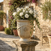 Image of sand glazed french anduze urn on a pillar in a european courtyard with a floral arrangement